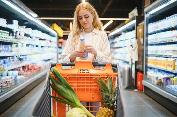Young adult woman pushing shopping trolley between the shelves in the market