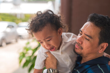 Fototapeta premium A dad tries to distract his young toddler son from crying, trying to pique his interest while carrying him around.