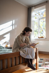Unsociable teen girl spending time alone at home in summer sunny day, scrolling social networks in...