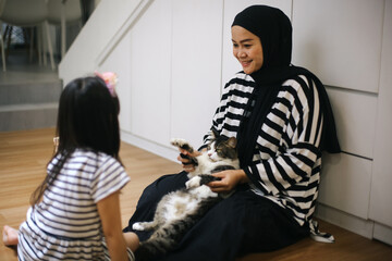 Young Muslim Mother And Daughter Playing With Cat At Home In Living Room