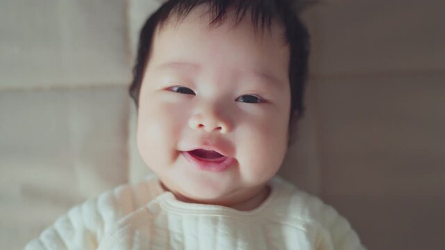 Top view - Adorable asian baby comfortable with delighted and smiling expression, Lying on a bed looking at camera. Baby healthcare hygiene concept.