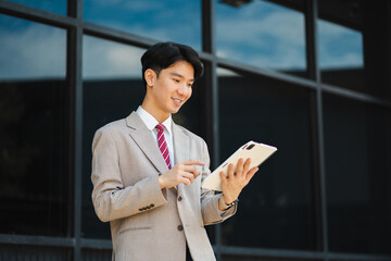 Fototapeta premium Professional businessman using digital tablet computer, smartphone and holding coffee to go while working at office.