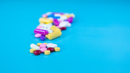 Group of colorful pills and capsules used in medical treatment, placed on blue background with blurred multi-colored pills. Medicine used in medical treatment. Healthcare and medicine concept.