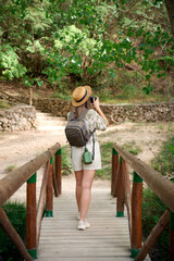 Young woman exploring nature while capturing moments on a wooden bridge in a lush forest