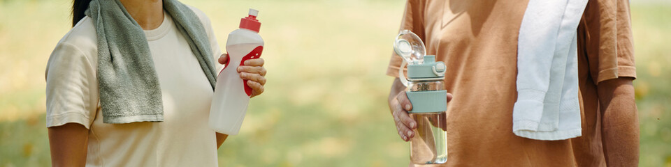 Two people staying hydrated in outdoor environment with light and relaxed ambiance, each holding...