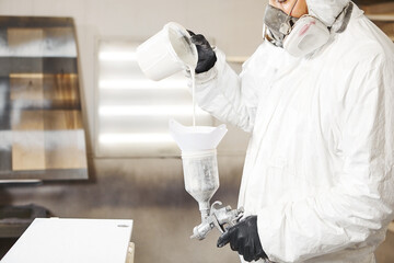 Man pours paint into the sprayer before painting the wood.