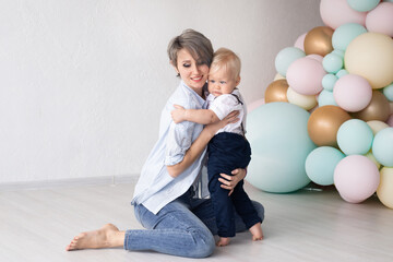 Happy family, mother with her baby boy at home on his first birthday in the background of colorful balloons.