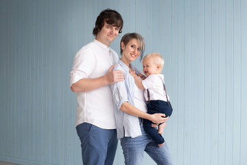 Happy parents mother and father with baby son on hands, near a blue wooden wall and smiling at home, happy family