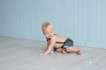 Messy baby boy after eating his birthday cake on his first birthday sitting on floor, smash cake party