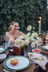A close-up of a plate of baked peach with buttercream and almonds. A covered festive table decorated with flowers and candles.