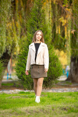 A young smiling girl walking in an autumn park in a good mood. Teenage girl, portrait against a background of nature. Fashion style trend.