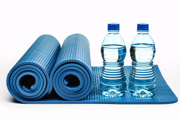 Two blue yoga mats rolled up with two bottles of water on a white background.