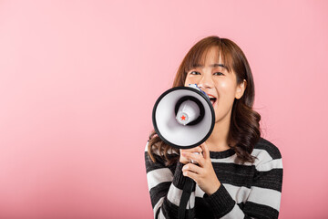 Fototapeta premium Portrait of happy Asian beautiful young woman teen confident smiling face holding making announcement message shouting screaming in megaphone, studio shot isolated on pink background, with copy space