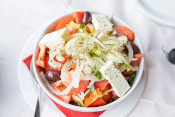 Fresh Greek Salad With Tomatoes, Cucumbers, Olives, Onions, And Feta Cheese, Beautifully Presented On A Rustic Restaurant Table. Perfect For Food And Culinary Themes
