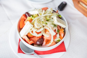Fresh Greek Salad With Tomatoes, Cucumbers, Olives, Onions, And Feta Cheese, Beautifully Presented On A Rustic Restaurant Table. Perfect For Food And Culinary Themes