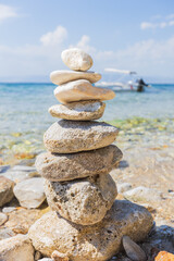Tranquil beach scene with stacked stones, clear water, and a boat in the background, perfect for relaxation and balance.