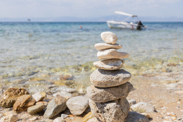 Tranquil beach scene with stacked stones, clear water, and a boat in the background, perfect for relaxation and balance.