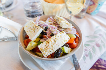 Fresh Greek Salad With Tomatoes, Cucumbers, Olives, Onions, And Feta Cheese, Beautifully Presented On A Rustic Restaurant Table. Perfect For Food And Culinary Themes