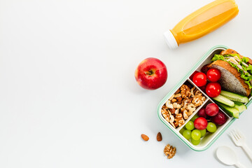Healthy lunchbox with sandwich, nuts, cherry tomatoes, cucumber slices, grapes, apple, and orange juice. Perfect for nutrition, wellness, and healthy lifestyle themes