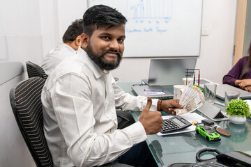 Indian loan applicant in the bank office giving a thumbs up, smiles broadly as he receives his loan...