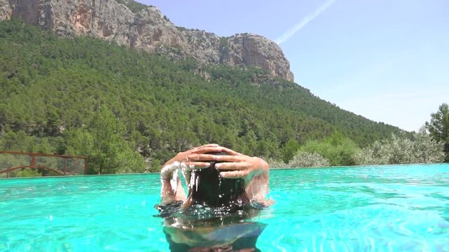 Woman emerging from clear water of blue swimming pool