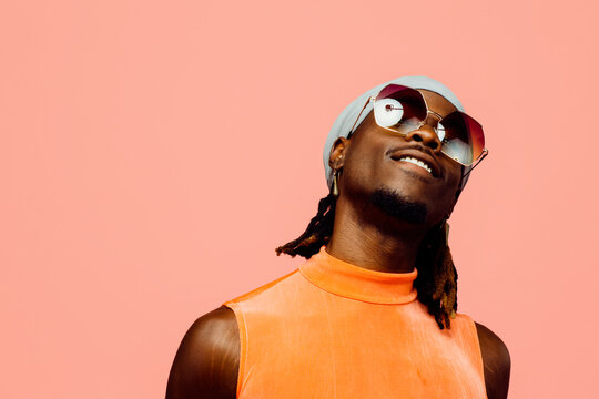 Portrait of a happy young man with sunglasses and cap laughing, isolated on pink