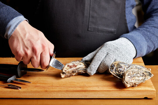 Man in apron shucking oysters on a wooden board