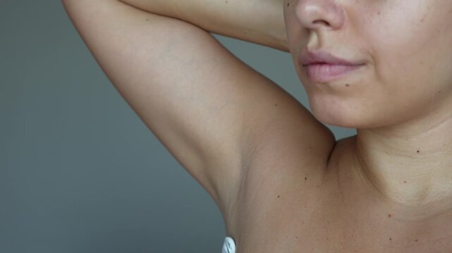 Cropped shot of a young woman shaving her armpit with a razor on a dark grey background. Getting rid of unwanted hair