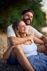 A couple laughing while sitting by the lake in a hug.