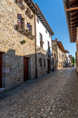 Quaint stone-paved street in Santillana del Mar, Spain, with rustic stone buildings and flower-adorned balconies. Ideal for travel, architecture, and cultural themes