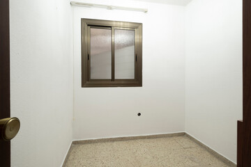 A simple, small empty room featuring a single window adorned with frosted glass, presenting an opportunity for imagination, design, and future use.