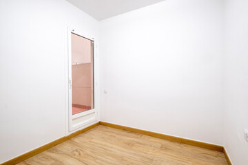An empty room with a single door leading outside, showcasing beautiful wooden flooring and white walls, ideal for design and home improvement ideas.