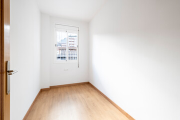 This image shows an empty room with light wooden flooring, a large window revealing urban buildings. The walls are white, and the space is clean and minimalist.