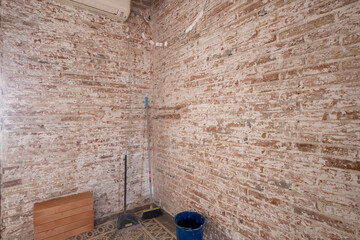 An indoor space currently undergoing renovation, showcasing exposed brick walls, construction materials, and tools, highlighting the transformation process.