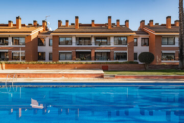 A luxurious residential complex featuring modern townhouses with terra cotta roofs and chimneys, and a large outdoor swimming pool, creating a serene living environment.