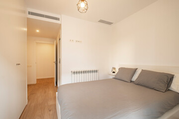A cozy bedroom featuring a minimalistic design, a comfortable bed with grey bedding, wooden flooring, a modern hanging lamp, and built-in storage for a relaxing atmosphere.