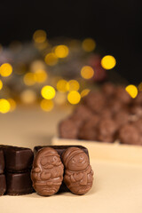 Chocolates in the shape of Christmas figures on the background of a flashing garland