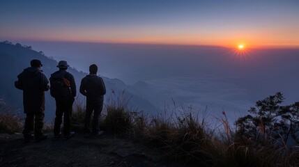 Three people are standing on a hillside, looking out at the sunset