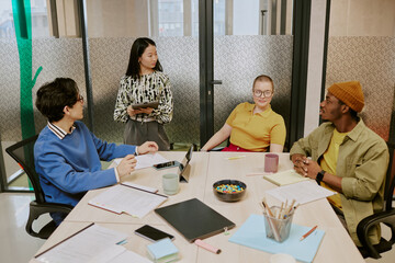 High angle view of young ethnically diverse gen Z colleagues working together on business plan in board room in office