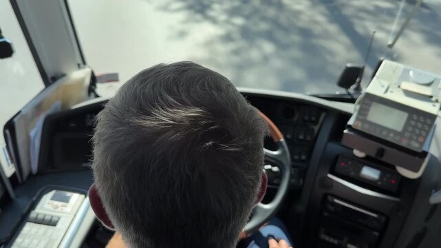 Bus driver head, defocussed coach controls, driving on the road; overhead view.