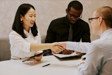Ethnically diverse female managers greeting each other with handshake while their male colleague...