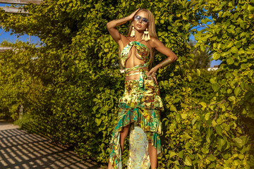 Sexy blonde model in floral print bikini and long elegant beach skirt with ruffles poses sensually...