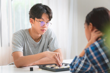 Asian teenage girl and boy playing board game, Asian brother and sister relaxing hobbies playing a game of checkers in living room