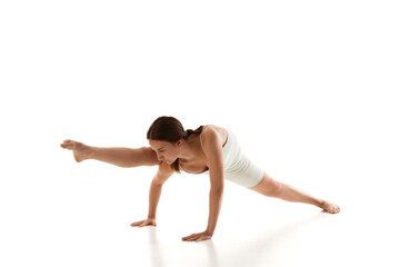 Woman in athletic wear performs challenging yoga pose showcasing strength and balance against white studio background. Concept of beauty, mindfulness, mental health, wellness, concentration. Ad