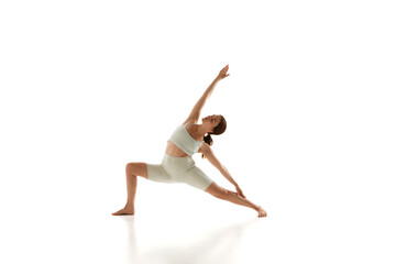 Woman in athletic wear performs yoga pose, stretching her legs, arms and back against white studio background. Healthy lifestyle. Concept of beauty, mindfulness, mental health, concentration. Ad