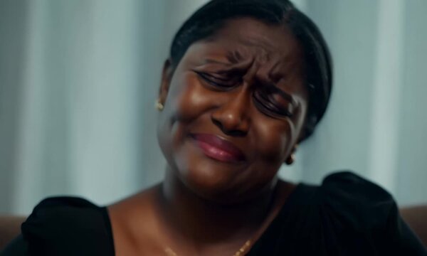A close-up shot of a black woman's face as she cries on a sofa in a living room