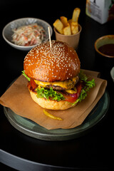 close up of burger with cheese and potatoes on a black table