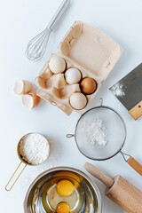 eggs in a tray, sieve, whisk, measuring cup, rolling pin, bowl with raw yolks lie on a light background