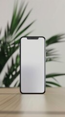 Modern smartphone with blank screen on wooden surface, green plants in background.