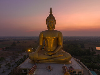 Obraz premium scenery sunset behind the great golden Buddha landmark of Thailand at wat Muang Ang Thong Thailand. .The largest Buddha statue in the world Surrounded by rice fields..colorful sky background.